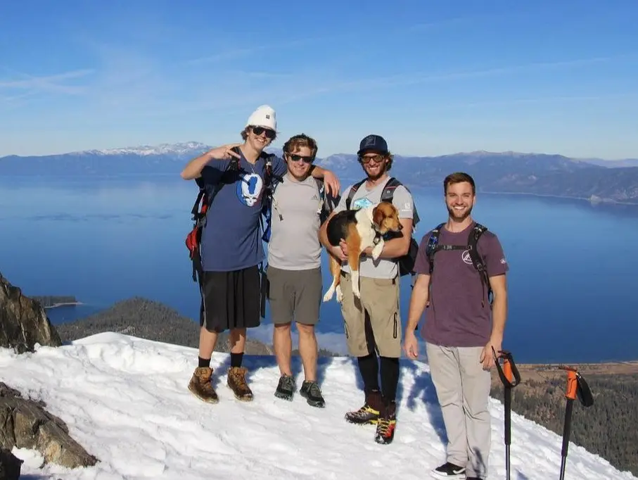 Guides posing with their dog on a snowy Mount Tallac summit overlooking Lake Tahoe